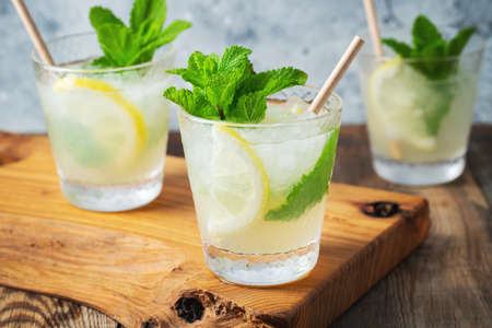 Two glass with lemonade or mojito cocktail with lemon and mint, cold refreshing drink or beverage with ice on rustic blue backgroundの写真素材