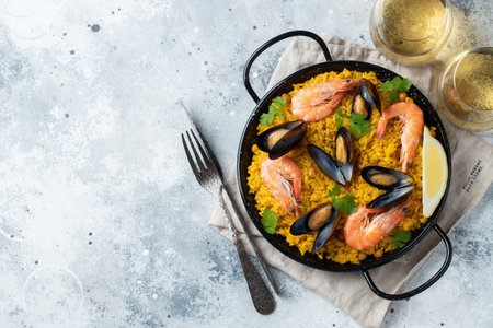 Traditional spanish seafood paella in pan with chickpeas, shrimps, mussels, squid on light grey concrete background. Top view with copy spaceの写真素材