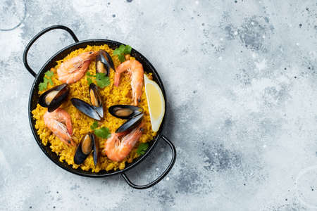 Traditional spanish seafood paella in pan with chickpeas, shrimps, mussels, squid on light grey concrete background. Top view with copy spaceの写真素材