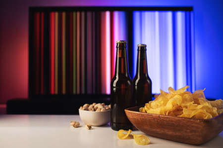 A wooden bowl of chips and snacks in the background the TV works. Evening cozy watching a movie or TV series at home with glass of beerの写真素材