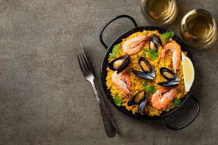 Traditional spanish seafood paella in pan with chickpeas, shrimps, mussels, squid on brown concrete background. Top view with copy spaceの写真素材