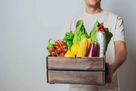 Delivery Concept -Young Caucasian delivery man carrying wooden box of grocery vegetables and fruits from store. Isolated on Grey studio Background. Copy Spaceの写真素材