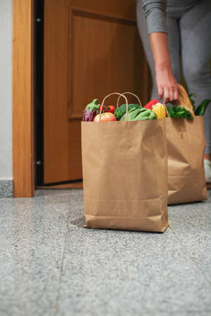 A woman picks up a bag of food at the door of her house. Quarantine. Stay at home, Online shopping. Vegetables and fruits delivery during quarantine and self-isolation.の写真素材