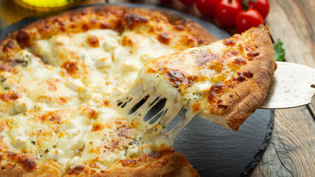 A slice of hot Italian pizza with stretching cheese. Pizza four cheeses with basil.の写真素材