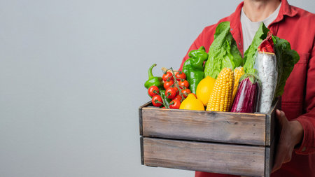 Delivery Concept -Young Caucasian delivery man carrying wooden box of grocery vegetables and fruits from store. Isolated on Grey studio Background. Copy Spaceの写真素材