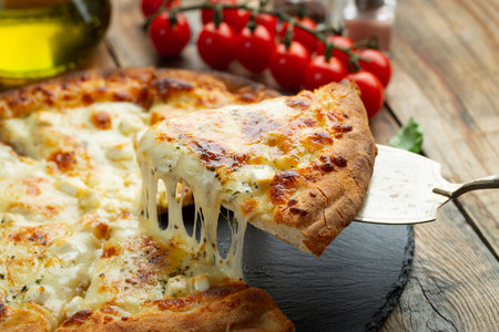A slice of hot Italian pizza with stretching cheese. Pizza four cheeses with basil on a wooden background.の写真素材