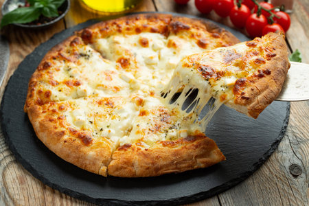 A slice of hot Italian pizza with stretching cheese. Pizza four cheeses with basil on a wooden background.の写真素材