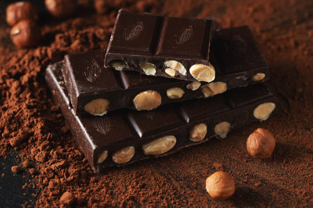 Dark and milk chocolate with nuts on a dark background sprinkled with cocoa powder.の写真素材