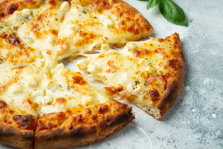 Italian pizza four cheeses with stretching cheese and basil on a light concrete background.の写真素材