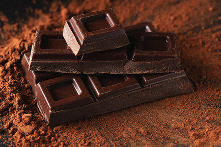 Dark and milk chocolate with nuts on a dark background sprinkled with cocoa powder. Chocolate pieces with almonds and hazelnuts close-up.の写真素材