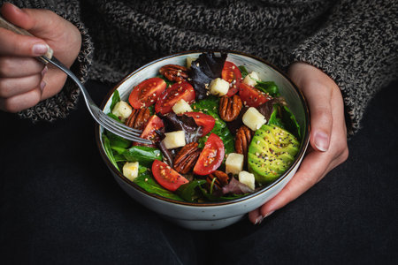 Healthy homemade salad with tomatoes, cheese cubes, pecans, avocado, spinach and arugula.の写真素材