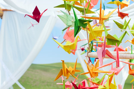 Bright origami cranes flutter in the wind in the field, creating an atmosphere of lightness, comfort and creativity in the open airの写真素材