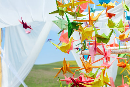 Bright origami cranes flutter in the wind in the field, creating an atmosphere of lightness, comfort and creativity in the open airの写真素材