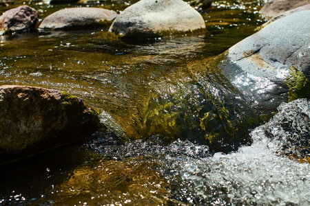 Close-up of a clear mountain stream in Boshkyzylsay, Uzbekistan, where water flows over smooth...