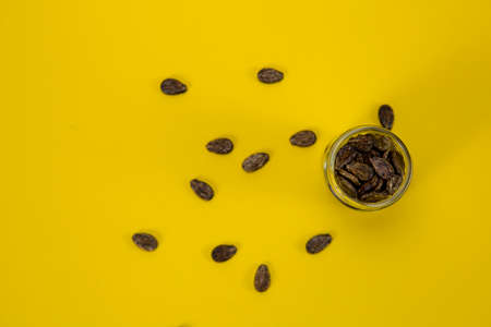 A jar of watermelon seeds, sprinkled around on a yellow backgroundの写真素材