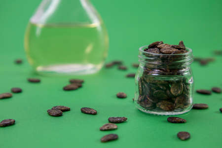 Watermelon oil from seeds in a bottle, seeds are scattered around, a jar full of seeds on a green backgroundの写真素材