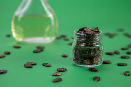 Watermelon oil from seeds in a bottle, seeds are scattered around, a jar full of seeds on a green backgroundの写真素材