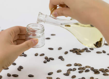 A hand pours watermelon oil into a jar, watermelon seeds are scattered on the table, close-up on a white backgroundの写真素材