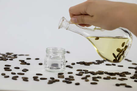 A hand pours watermelon oil into a jar, watermelon seeds are scattered on the table, close-up on a white backgroundの写真素材