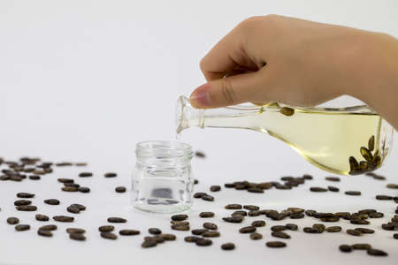 A hand pours watermelon oil into a jar, watermelon seeds are scattered on the table, close-up on a white backgroundの写真素材