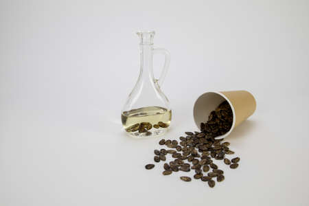 Watermelon seed oil in a bottle, watermelon seeds pour out of an eco glass on the table on a white BGの写真素材