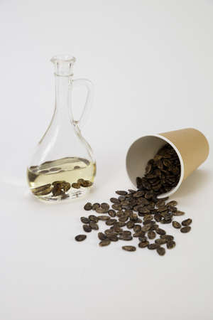 Watermelon seed oil in a bottle, watermelon seeds pour out of an eco glass on the table on a white BGの写真素材