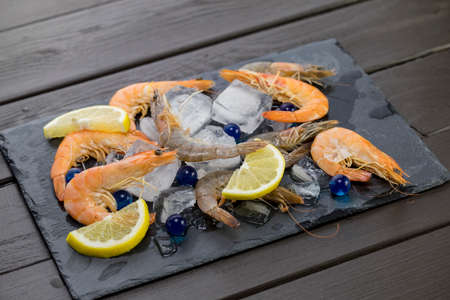 shrimp on a stone plate with ice, on the bg of a wooden tableの写真素材