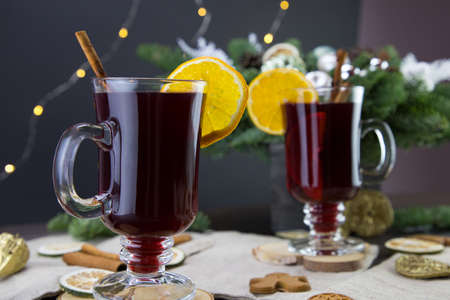 Mugs of warm wine with orange, cookies and cinnamon, dried fruit and spruce branches, Traditional hot drink for Christmas, close-up shot of warm wine.の写真素材