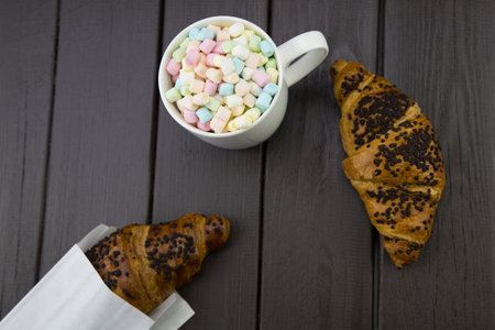 morning breakfast with a mug of coffee and marshmallow, and a chocolate croissant on a wooden boardの写真素材