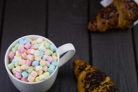 morning breakfast with a mug of coffee and marshmallow, and a chocolate croissant on a wooden boardの写真素材