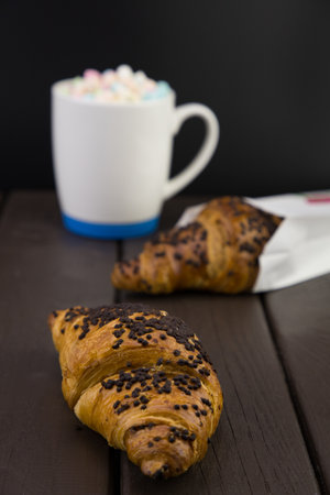morning breakfast with a mug of coffee and marshmallow, and a chocolate croissant on a wooden boardの写真素材