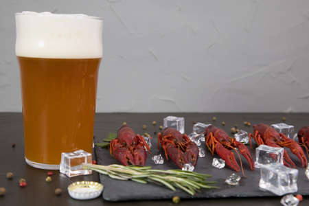 Delicious boiled crayfish close-up on a stone plate, around pieces of ice, and with a glass of beer, with pepper, lemon and parsley. Black backgroundの写真素材