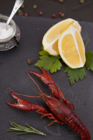 Delicious boiled crayfish close-up on a stone plate with pepper, lemon and parsley.の写真素材