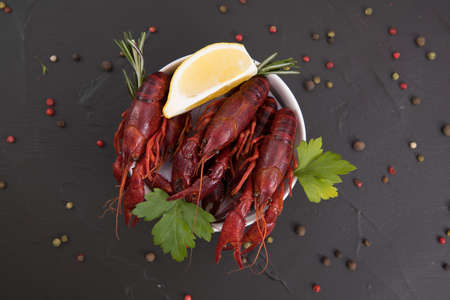 Delicious boiled crayfish close-up on a stone plate with pepper, lemon and parsley. free space for your text. Black background.の写真素材