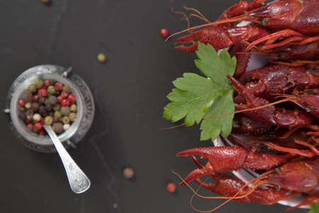 Delicious boiled crayfish close-up on a stone plate with pepper, lemon and parsley. free space for your text. Black background.の写真素材