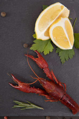Delicious boiled crayfish close-up on a stone plate with pepper, lemon and parsley.の写真素材