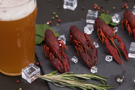 Delicious boiled crayfish close-up on a stone plate, around pieces of ice, and with a glass of beer, with pepper, lemon and parsley. Black backgroundの写真素材