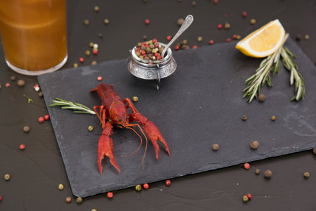 Delicious boiled crayfish close-up on a stone plate, around pieces of ice, and with a glass of beer, with pepper, lemon and parsley. Black backgroundの写真素材