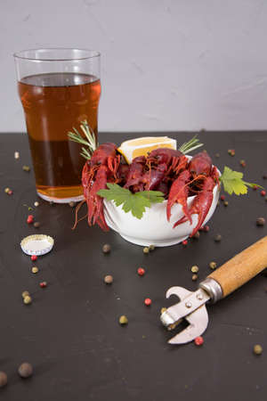 Delicious boiled crayfish close-up on a stone plate, around pieces of ice, and with a glass of beer, with pepper, lemon and parsley. Black backgroundの写真素材
