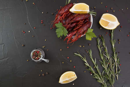 Delicious boiled crayfish close-up on a stone plate with pepper, lemon and parsley. free space for your text. Black background.の写真素材