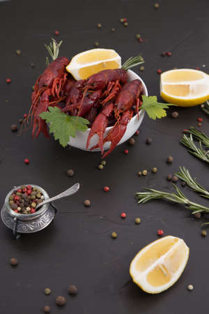 Delicious boiled crayfish close-up on a stone plate with pepper, lemon and parsley. free space for your text. Black background.の写真素材