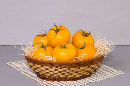 yellow tomatoes in the basket, on gray background.の写真素材