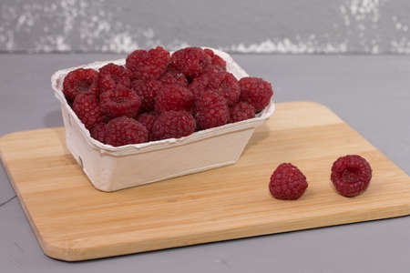 Raspberries in cardboard box on a wooden table.の写真素材