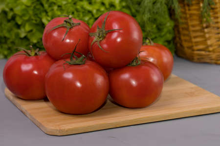 Red tomatoes with green salad, on brown wooden desk and gray background.の写真素材