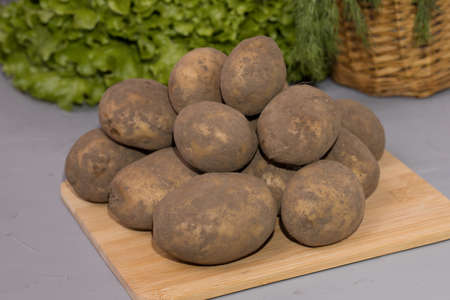 Fresh potatoes on a wooden board, on a green salad background.の写真素材