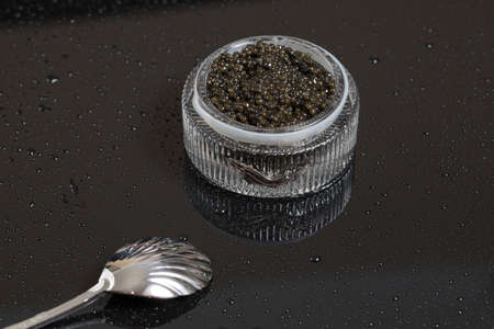 Black caviar in a bowl, on a black surface with a caviar spoon.の写真素材