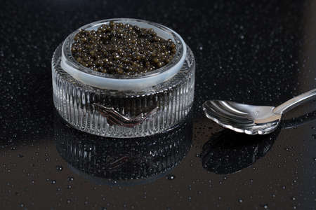 Black caviar in a bowl, on a black surface with a caviar spoon.の写真素材