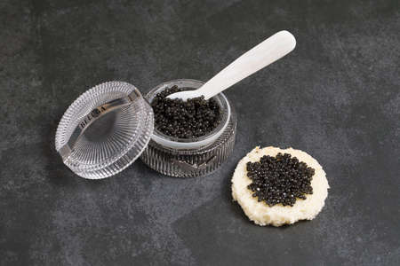 Black caviar in a bowl, and caviar on white bread, on a black surface with a caviar spoonの写真素材