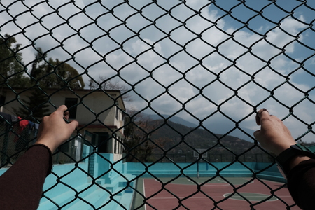 Hands on a grid in the background of a basketball court with a view of the mountainsの写真素材