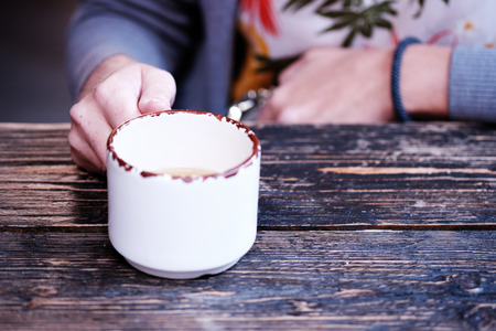 Girl hand with a mug on the background of a wooden tableの写真素材